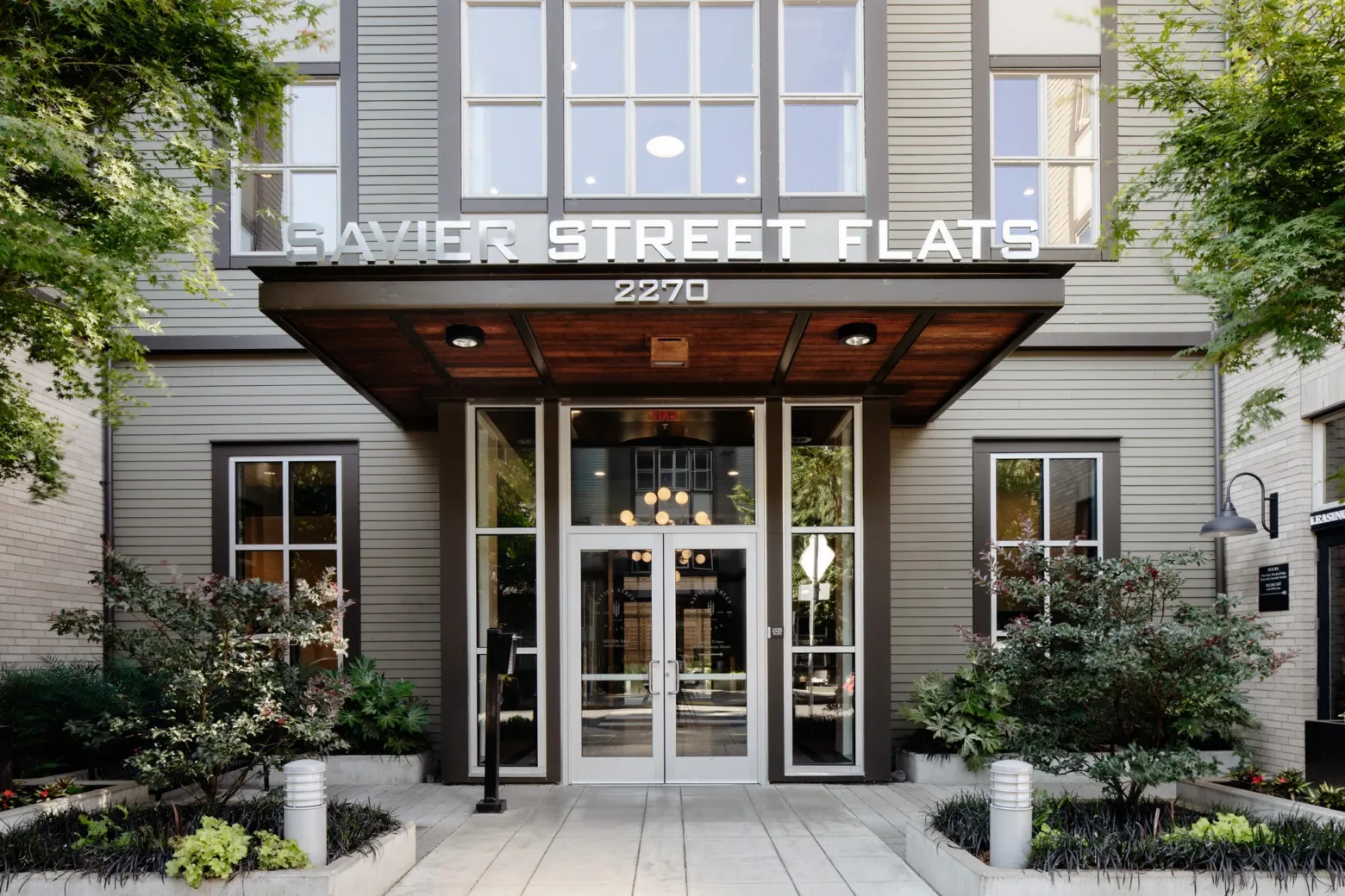 Front exterior of Savier Street Flats, featuring a modern entrance with large glass doors, surrounded by landscaped greenery and trees.