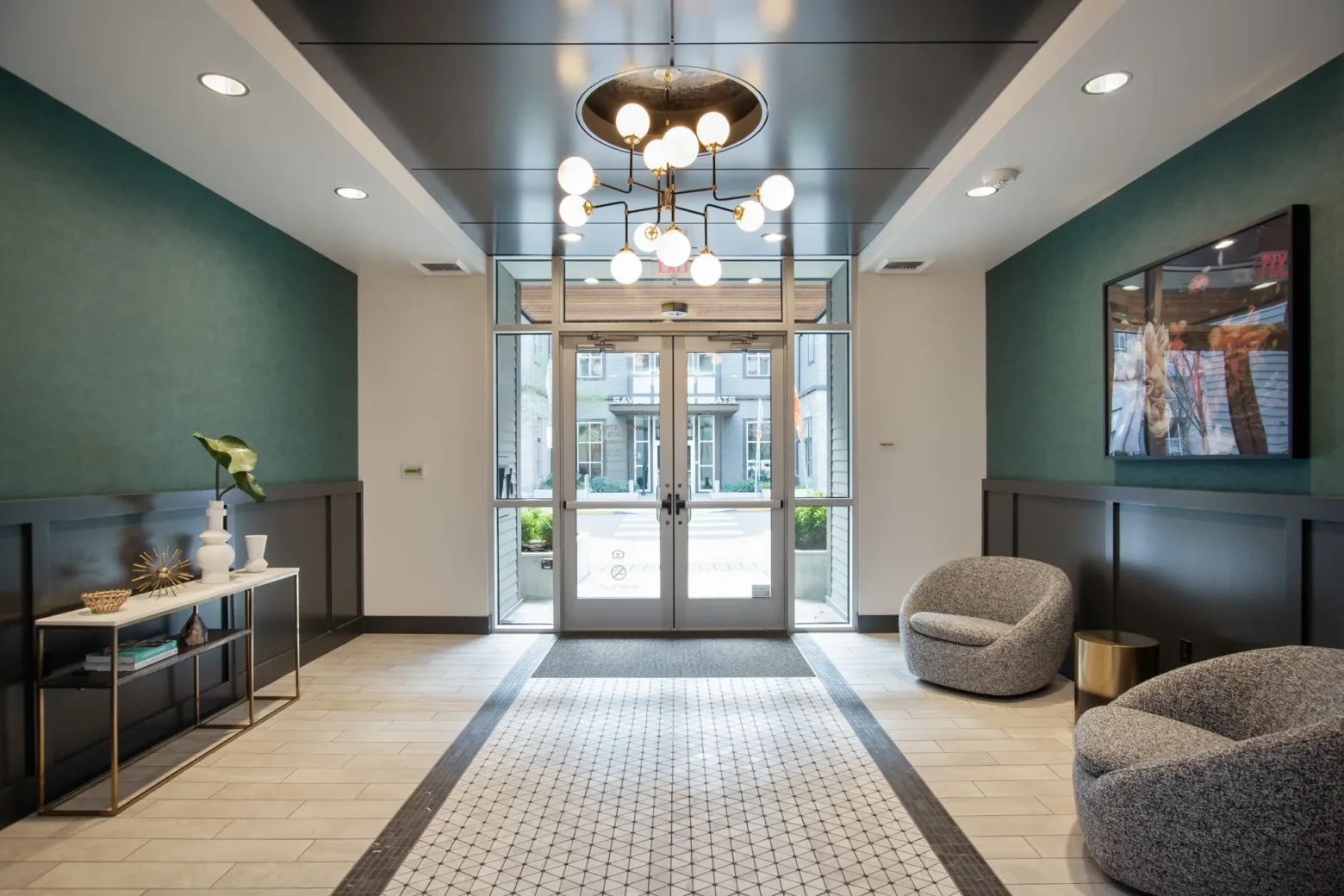 Modern lobby with elegant lighting, patterned rug, and stylish seating. Console table holds decorative vases. Glass doors reveal an outdoor courtyard.