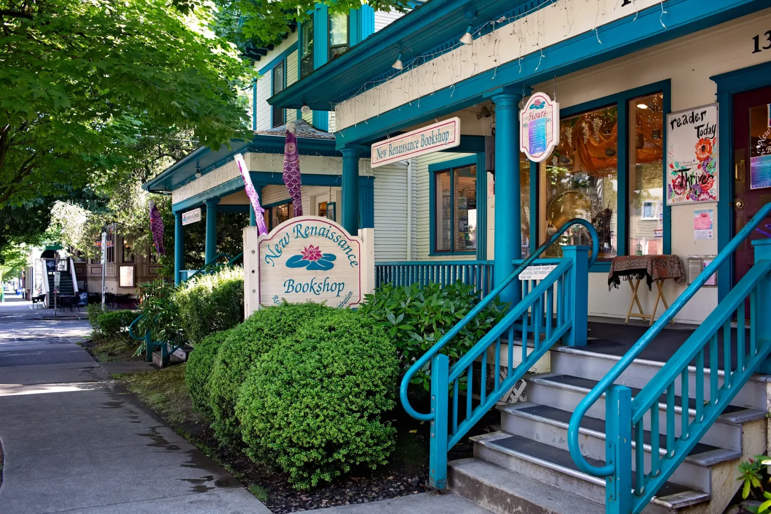 The image features the New Renaissance Bookshop with a vibrant, inviting entrance, surrounded by greenery and colorful signage on a sunny day.