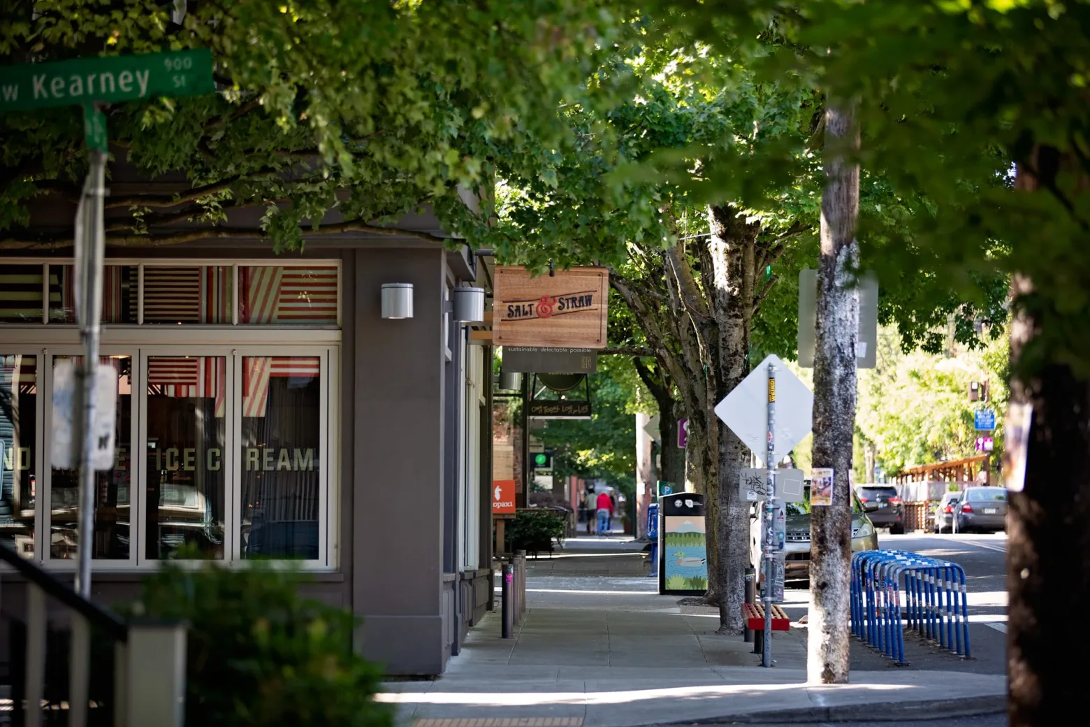 Tree-lined street with a person walking, bike racks, and the Salt & Straw ice cream shop on Northwest Kearney Street.