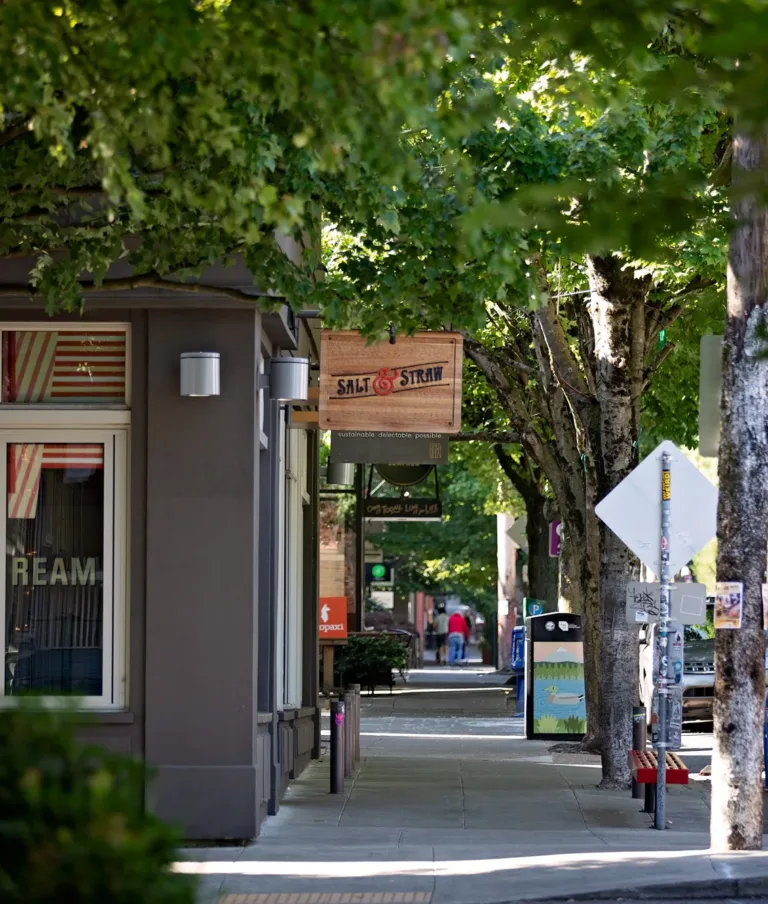 Tree-lined street with a person walking, bike racks, and the Salt & Straw ice cream shop on Northwest Kearney Street.