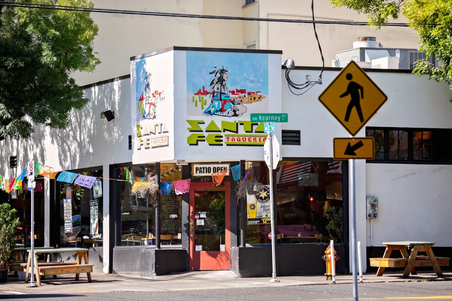 A colorful taqueria with festive banners, located at NW Kearney St. A pedestrian crossing sign is visible in the foreground.