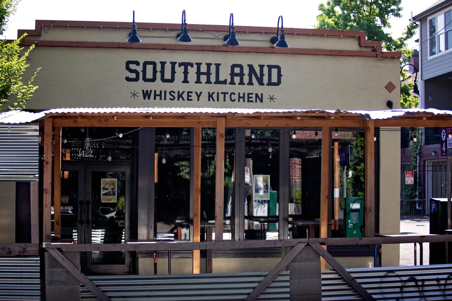 Wooden-framed, rustic-style restaurant exterior with "Southland Whiskey Kitchen" sign. Large windows reflect outdoor greenery. No visible persons.