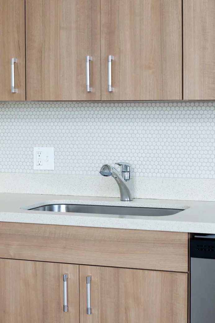 Apartment kitchen with wooden cabinets, stainless steel sink, and a hexagonal tile backsplash.
