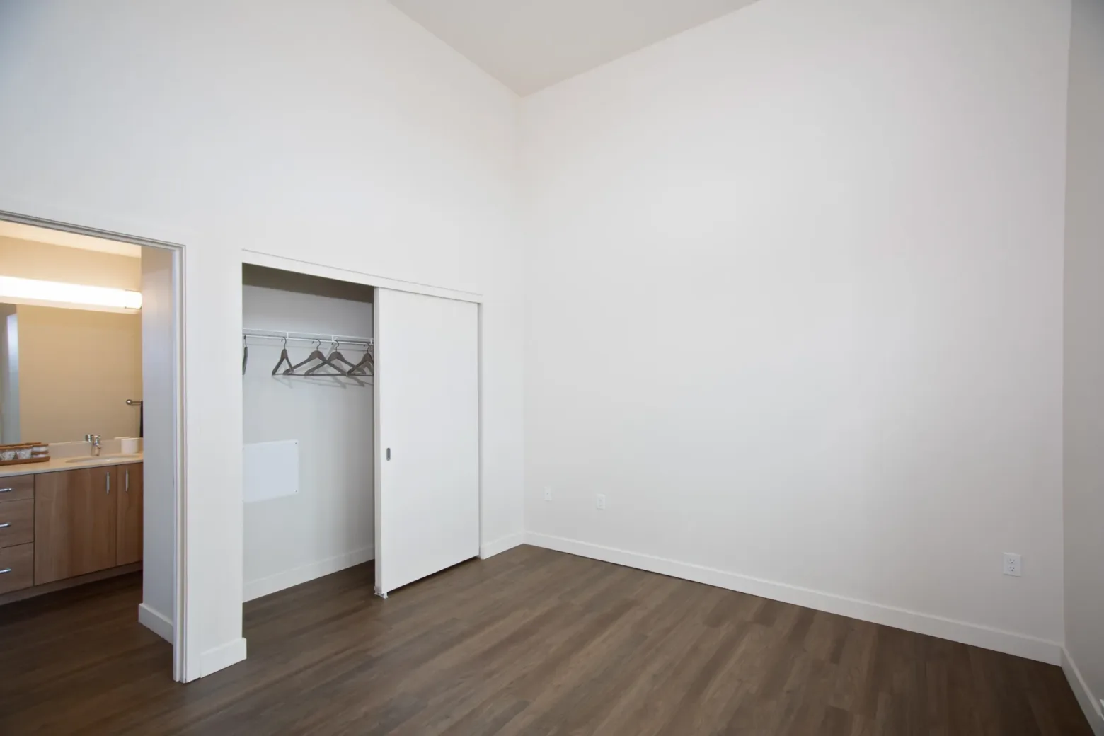 Empty apartment room with wood flooring, white walls, and an open closet with hangers under soft lighting.