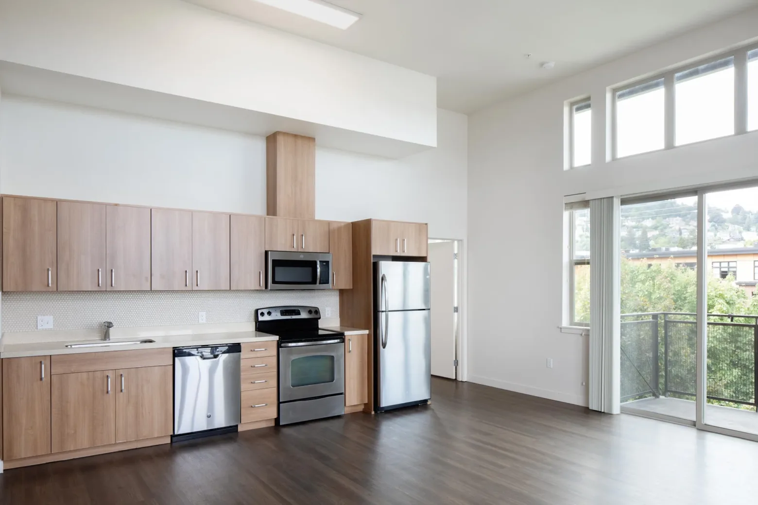 Modern apartment kitchen with wooden cabinets, stainless steel appliances, and large windows.