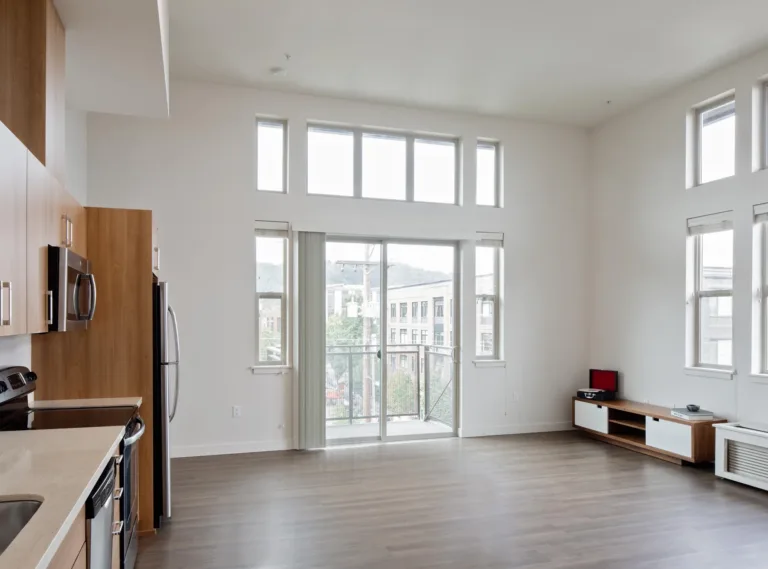 Spacious modern apartment with large windows and a balcony, featuring a kitchen area with wooden cabinets and stainless steel appliances.