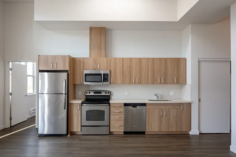 Modern kitchen with wooden cabinets, stainless steel appliances, and white countertops. Includes a fridge, stove, dishwasher, and microwave, with ample overhead storage.