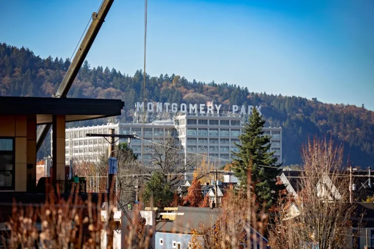 A view of the Montgomery Park building with large letters spelling "MONTGOMERY PARK" on the rooftop, surrounded by trees and hills in the background, under a clear blue sky.