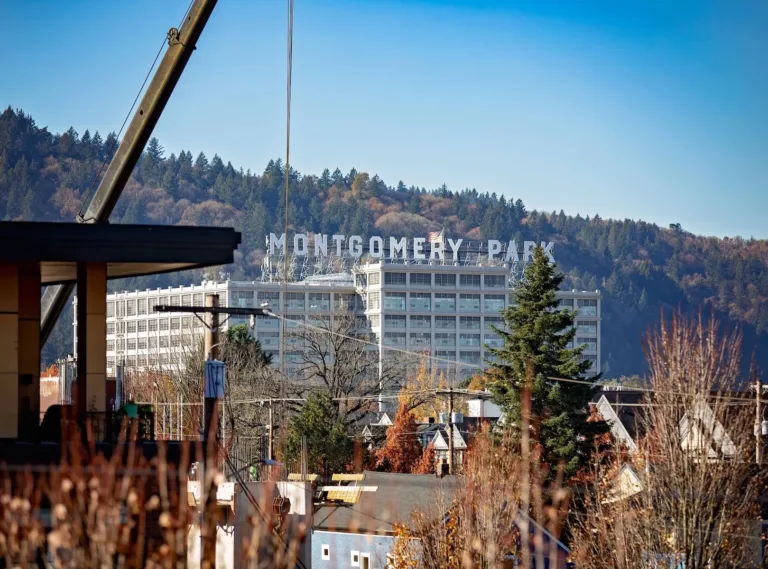 A view of the Montgomery Park building with large letters spelling "MONTGOMERY PARK" on the rooftop, surrounded by trees and hills in the background, under a clear blue sky.