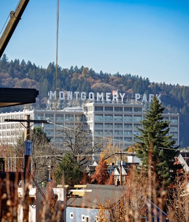 A view of the Montgomery Park building with large letters spelling "MONTGOMERY PARK" on the rooftop, surrounded by trees and hills in the background, under a clear blue sky.