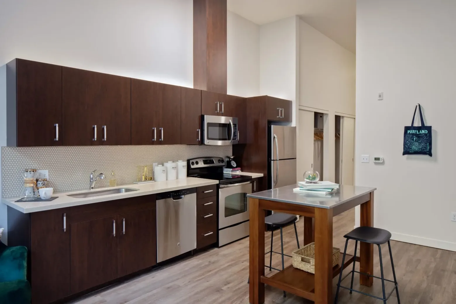 Modern kitchen with dark wood cabinets, stainless steel appliances, and a small dining table with stools in an apartment setting.