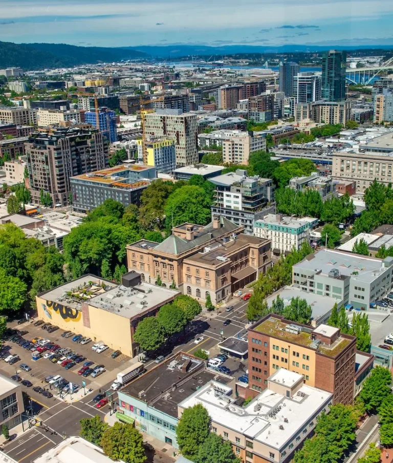 Aerial view of Portland, Oregon, featuring the Fremont Bridge, surrounded by urban buildings, lush green trees, and bustling city streets.