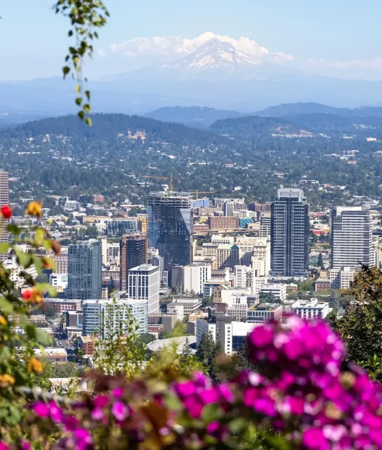 Skyline view of Portland, Oregon, adorned with flowers. Mount Hood looms in the background under clear skies, flanked by lush greenery.